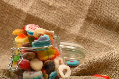 Kaba ev yapımı kumaşın arka planında cam bir kavanozda çok renkli marmelat. Lezzetli tatil hediyesi..