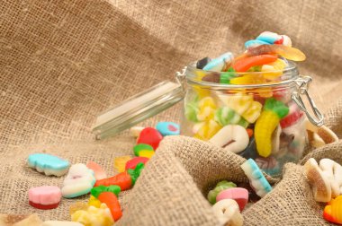 Kaba ev yapımı kumaşın arka planında cam bir kavanozda çok renkli marmelat. Lezzetli tatil hediyesi..