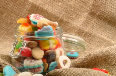 Kaba ev yapımı kumaşın arka planında cam bir kavanozda çok renkli marmelat. Lezzetli tatil hediyesi..