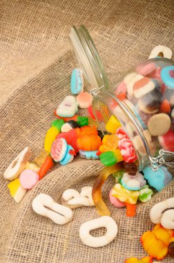 Kaba ev yapımı kumaşın arka planında cam bir kavanozda çok renkli marmelat. Lezzetli tatil hediyesi..