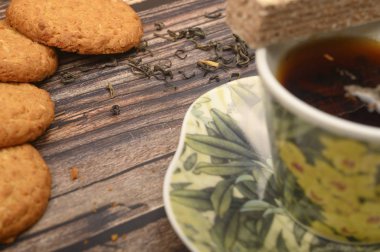 Bir fincan siyah çay, çay yaprağı, esmer şeker, yulaf ezmeli kurabiye, ahşap zemin üzerinde waffle. Kapat..