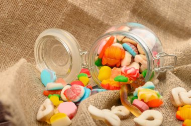 Kaba ev yapımı kumaşın arka planında cam bir kavanozda çok renkli marmelat. Lezzetli tatil hediyesi..