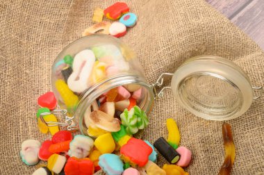 Kaba ev yapımı kumaşın arka planında cam bir kavanozda çok renkli marmelat. Lezzetli tatil hediyesi..