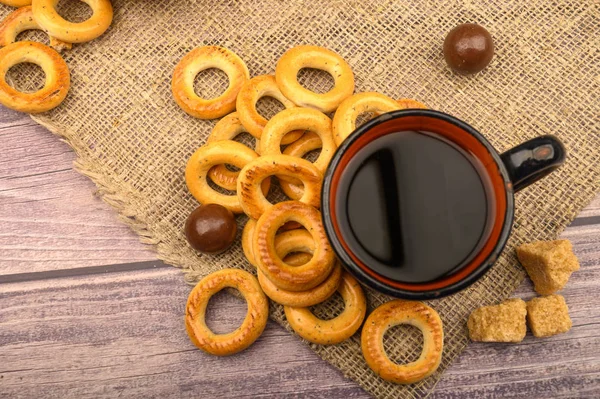 Pequenos bagels, chocolates, uma caneca de chá e um pano áspero em casa em um fundo de madeira close-up . — Fotografia de Stock