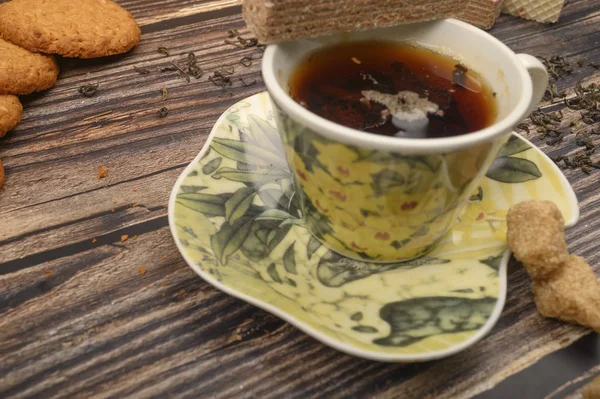 Eine Tasse schwarzen Tee, Teeblätter, braunen Zucker, Haferflockenkekse, Waffeln auf einem hölzernen Hintergrund. Nahaufnahme. — Stockfoto