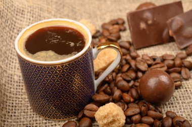 Bir fincan kahve, kahve çekirdekleri, kaba ev yapımı kumaşlı esmer şeker ve çikolata. Kapat..