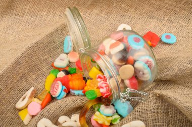 Kaba ev yapımı kumaşın arka planında cam bir kavanozda çok renkli marmelat. Lezzetli tatil hediyesi..