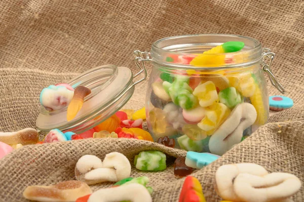 Kaba ev yapımı kumaşın arka planında cam bir kavanozda çok renkli marmelat. Lezzetli tatil hediyesi..