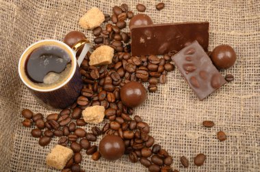 Bir fincan kahve, kahve çekirdekleri, kaba ev yapımı kumaşlı esmer şeker ve çikolata. Kapat..
