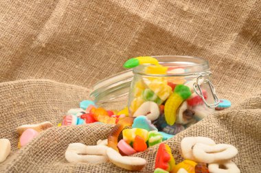 Kaba ev yapımı kumaşın arka planında cam bir kavanozda çok renkli marmelat. Lezzetli tatil hediyesi..