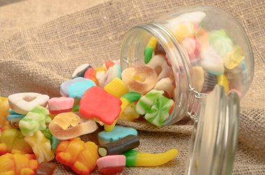 Kaba ev yapımı kumaşın arka planında cam bir kavanozda çok renkli marmelat. Lezzetli tatil hediyesi..