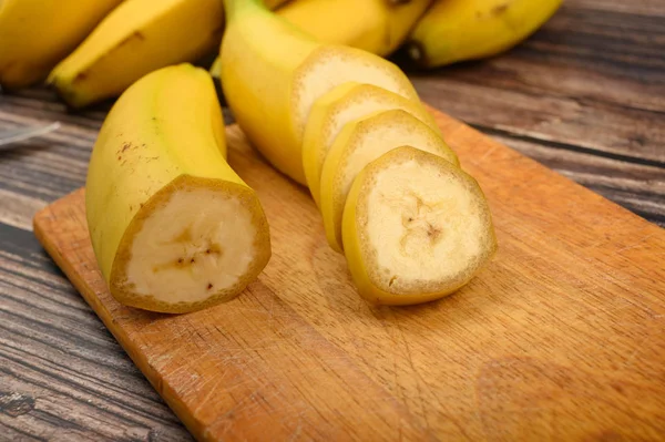 One ripe yellow banana cut into several pieces on a wooden Board on a wooden background. Close up. — Stock Photo, Image
