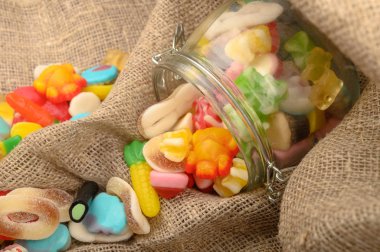 Kaba ev yapımı kumaşın arka planında cam bir kavanozda çok renkli marmelat. Lezzetli tatil hediyesi..