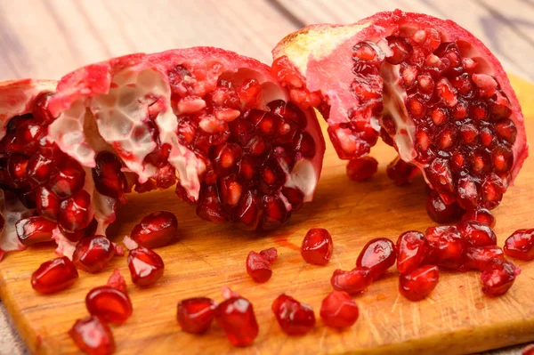 Pieces of ripe juicy pomegranate and pomegranate seeds on a wooden Board on a wooden background. Close up. — 스톡 사진