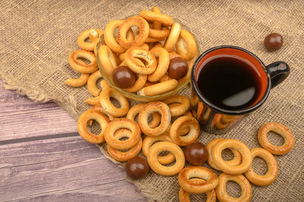 Pequenos bagels, chocolates, uma caneca de chá e um pano áspero em casa em um fundo de madeira close-up . — Fotografia de Stock