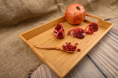 Olgun sulu nar, nar dilimleri ve tahta bir arka planda tahta bir tepside tahta bir kaşıkta nar tohumları. Kapat..