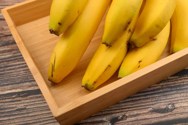 Куча спелых желтых бананов на деревянном подносе на деревянном фоне. Закрыть . — стоковое фото