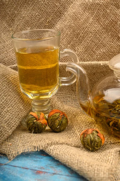 Thé aux fleurs versé dans un verre et quelques boules de thé aux fleurs sur un fond de tissu brut fait maison. Gros plan . — Photo