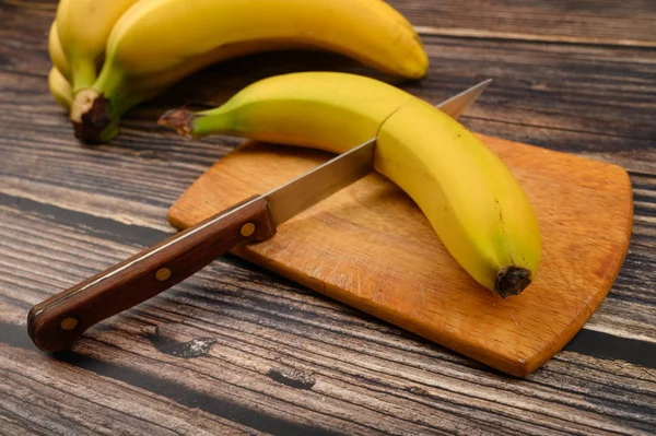 Один спелый желтый банан, разрезанный пополам ножом на деревянной доске на деревянном фоне. Закрыть . — стоковое фото