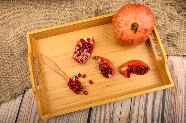 Reifen saftigen Granatapfel, Granatapfelscheiben und Granatapfelkerne in einem Holzlöffel auf einem hölzernen Tablett auf einem hölzernen Hintergrund. Nahaufnahme. — Stockfoto