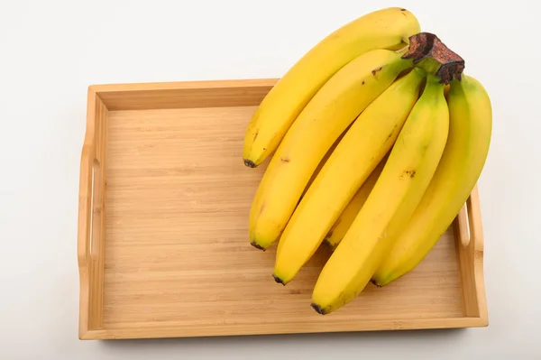 Куча спелых желтых бананов на деревянном подносе на белом фоне. Закрыть . — стоковое фото