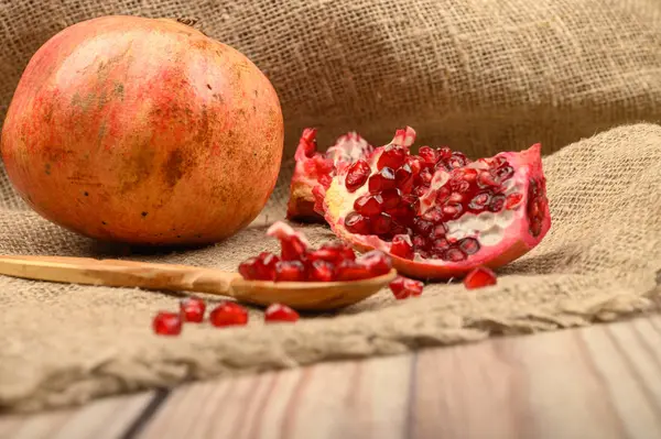 Einen reifen, saftigen Granatapfel und Granatapfelkerne in einem Holzlöffel auf einem Hintergrund aus grobem, selbst gesponnenem Stoff. Nahaufnahme. — Stockfoto