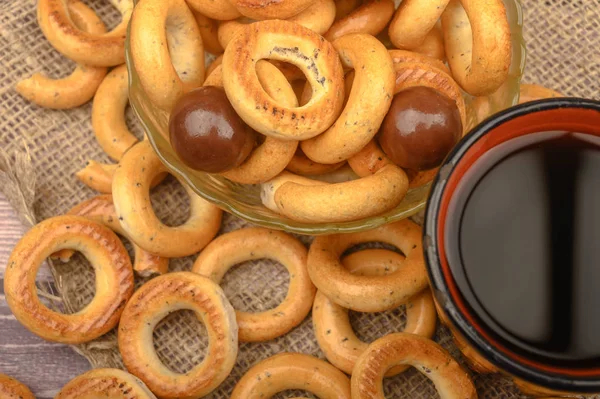 Kleine bagels, chocolaatjes, een mok thee en een ruwe homespun doek op een houten achtergrond close-up. — Stockfoto