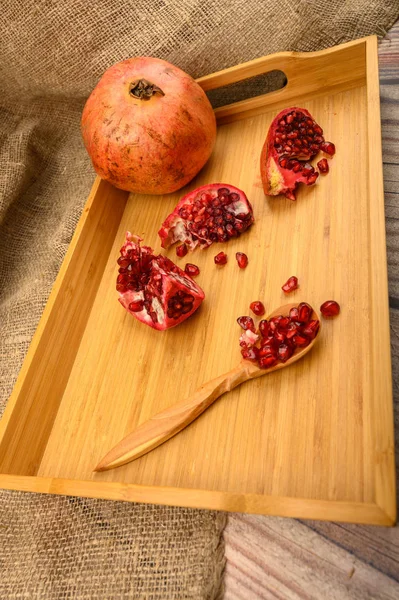 Reifen saftigen Granatapfel, Granatapfelscheiben und Granatapfelkerne in einem Holzlöffel auf einem hölzernen Tablett auf einem hölzernen Hintergrund. Nahaufnahme. — Stockfoto