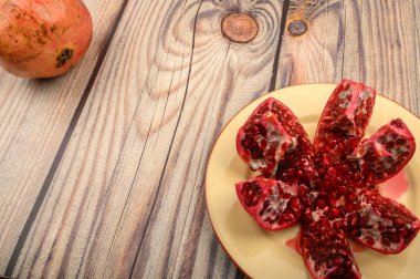 Olgun sulu nar, ahşap bir arka planda seramik bir tabakta birkaç parçaya bölünmüş. Kapat..