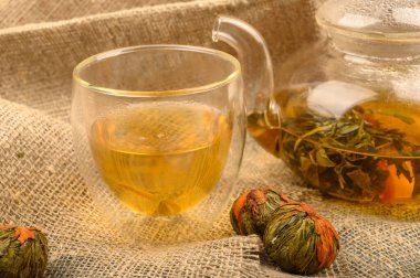 Cam çaydanlıkta demlenmiş çiçek çayı, bir bardak çay ve kaba ev yapımı kumaştan yapılmış bir fındık çiçeği çayı. Kapat..