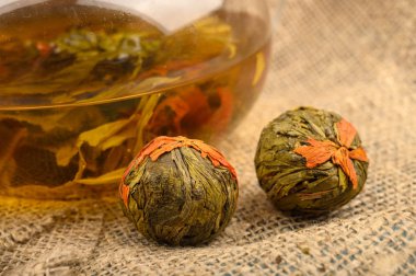 Cam çaydanlıkta demlenmiş çiçek çayı ve kabataslak ev yapımı kumaştan yapılmış çay topları. Kapat..