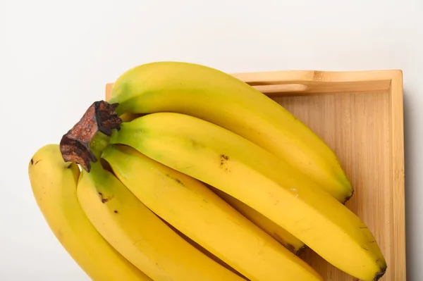 Куча спелых желтых бананов на деревянном подносе на белом фоне. Закрыть . — стоковое фото