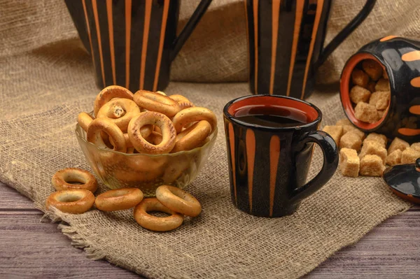 Pequenos bagels, açúcar mascavo, uma caneca de chá e pratos cerâmicos em um fundo de tecido caseiro áspero close-up . — Fotografia de Stock