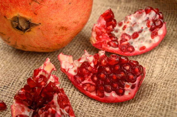 Ripe juicy pomegranate, pieces of pomegranate on the background of rough homespun fabric. Close up. — Stock Photo, Image