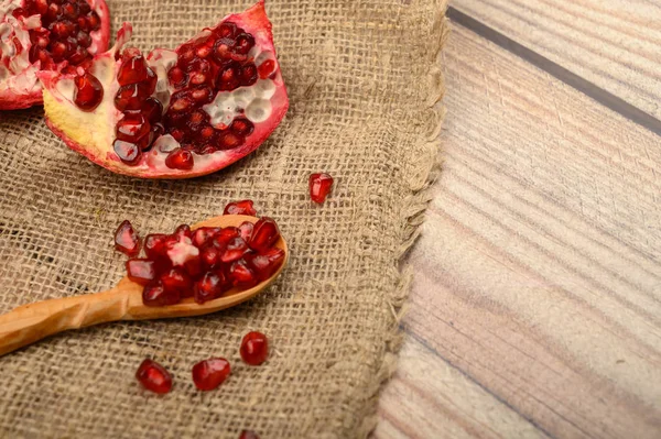 Stücke von saftigen reifen Granatapfel- und Granatapfelkernen auf einem Holzlöffel auf einem Hintergrund aus grobem selbstgesponnenem Stoff. Nahaufnahme. — Stockfoto