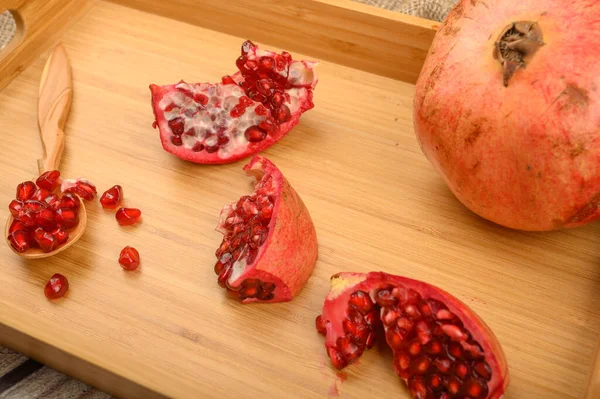 Reifen saftigen Granatapfel, Granatapfelscheiben und Granatapfelkerne in einem Holzlöffel auf einem hölzernen Tablett auf einem hölzernen Hintergrund. Nahaufnahme. — Stockfoto