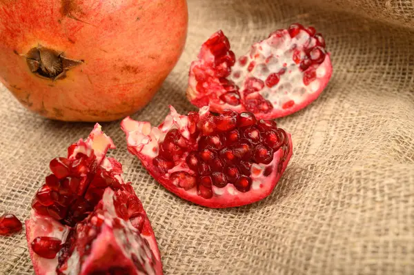 Reife saftige Granatäpfel, Granatapfelstücke und Granatapfelkerne auf einem Hintergrund aus grobem, selbst gesponnenem Stoff. Nahaufnahme. — Stockfoto