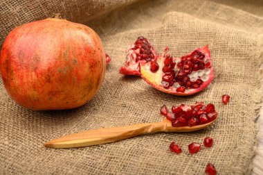 Olgun sulu nar, bir parça nar ve nar tohumu kaba ev yapımı kumaştan yapılmış ahşap bir kaşık üzerinde. Kapat..