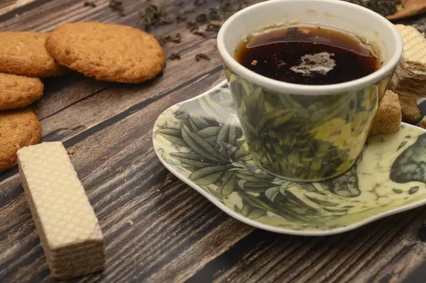 Eine Tasse schwarzen Tee, Teeblätter, braunen Zucker, Haferflockenkekse, Waffeln auf einem hölzernen Hintergrund. Nahaufnahme. — Stockfoto