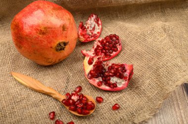 Olgun sulu nar, bir parça nar ve nar tohumu kaba ev yapımı kumaştan yapılmış ahşap bir kaşık üzerinde. Kapat..