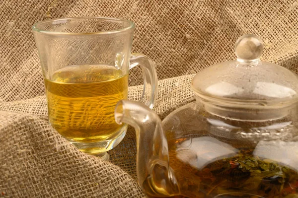 Thé de fleur infusé dans une théière en verre et un verre de thé de fleur sur un fond de tissu brut à la maison. Gros plan . — Photo