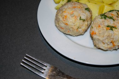 Kaynamış patatesli iki köfte ve siyah arka planda çatalı olan beyaz bir tabakta haşlanmış havuç. Kapat..