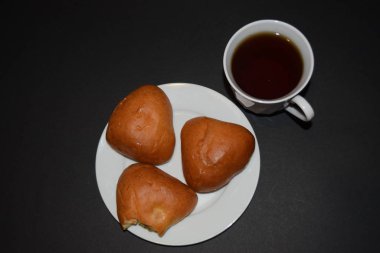 Beyaz tabakta üç turta ve siyah arka planda bir fincan kahve. Yukarıdan yakın görüntü.