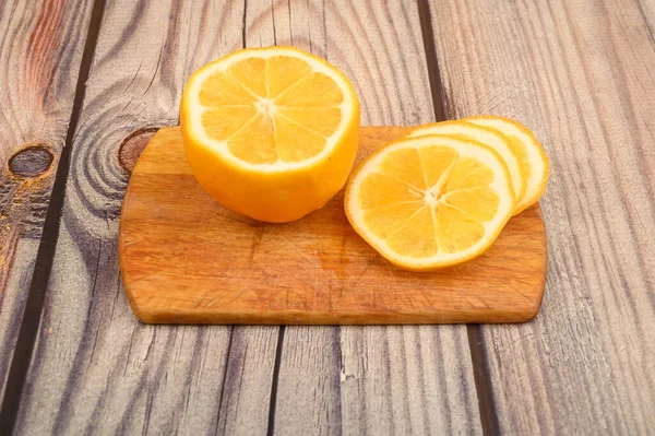 Gesneden rijpe gele citroen op een plank op een houten achtergrond. Sluiten.. — Stockfoto