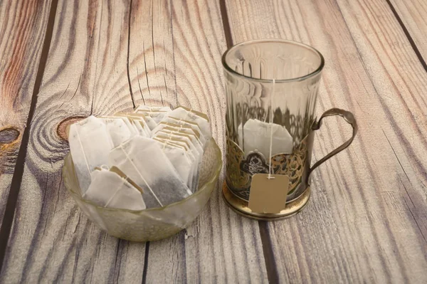 Tea bags in a glass vase and an empty faceted glass in a vintage Cup holder on a wooden background. Close up. — Stock Photo, Image