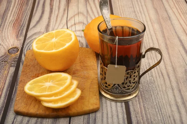 Чай в огранённом стекле в винтажном держателе Чаши, нарезанный лимон на доске на деревянном фоне. Закрыть . — стоковое фото