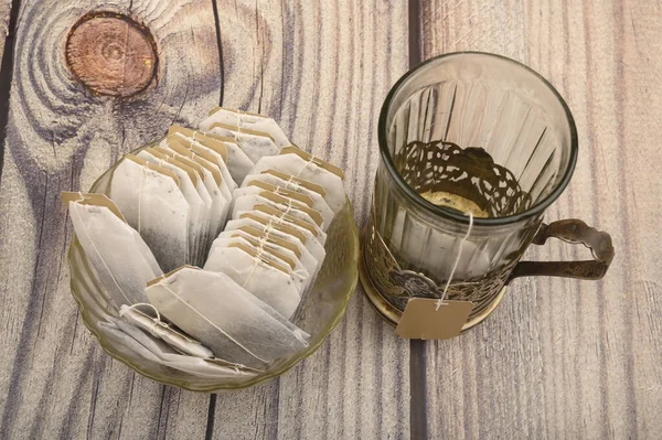 Tea bags in a glass vase and an empty faceted glass in a vintage Cup holder on a wooden background. Close up. — Stock Photo, Image