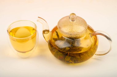 Cam çaydanlıkta demlenmiş çiçek çayı ve beyaz arka planda bir bardak çay. Kapat..