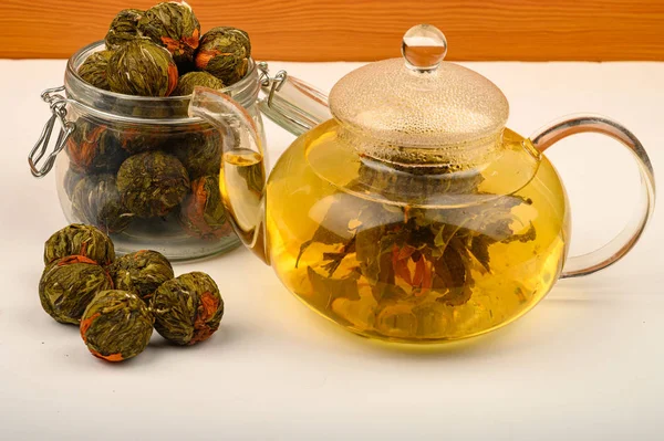 Tè di fiori preparato in una teiera di vetro, palle di tè di fiori e un barattolo di tè su uno sfondo bianco. Da vicino. . — Foto Stock