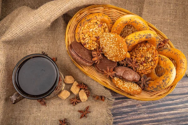 Cookies, chocolate cakes, bagels in a wicker basket and a glass of tea in a vintage Cup holder against a background of rough homespun fabric. Close up